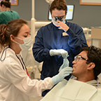 student in robes and face masks working on dental patient