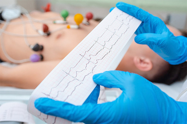 person wearing gloves examines ekg readout with patient attached to leads in background