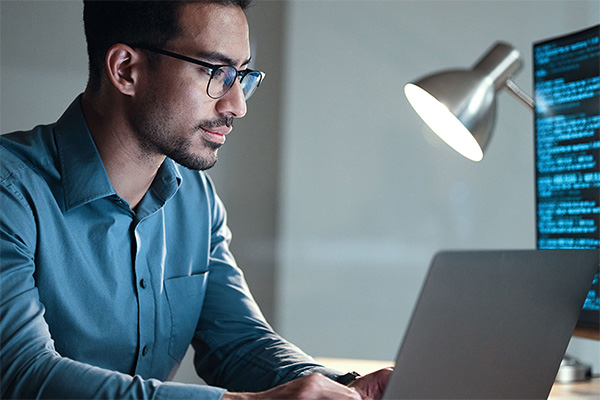 person working at laptop and looking at code on monitor screens