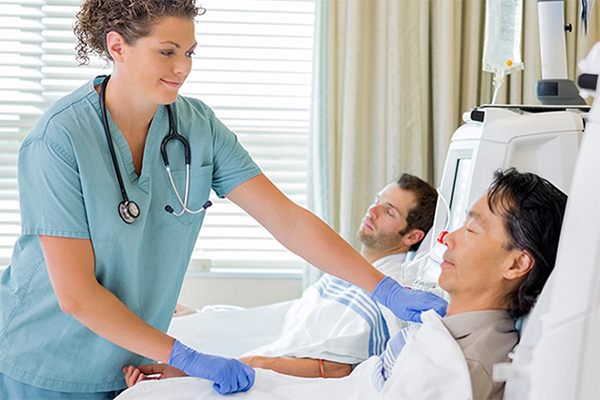 hemodialysis technician assists two patients in hospital beds receiving dialysis