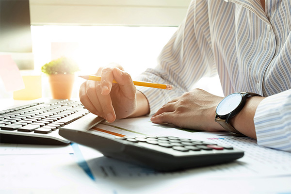 a person's hands, holding a pencil, above a keyboard and paper forms