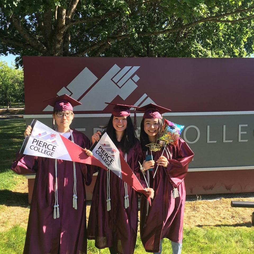 three students in graduation caps and gowns in front of pierce college sign