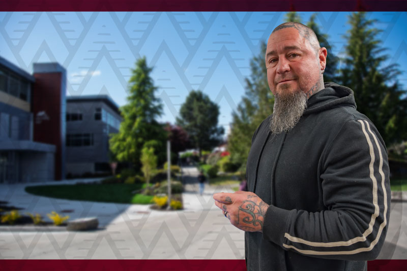 a student stands in front of a patterned background with a campus building in the background