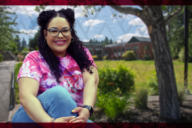 a smiling student sits outdoors with the pierce college puyallup quad in the background