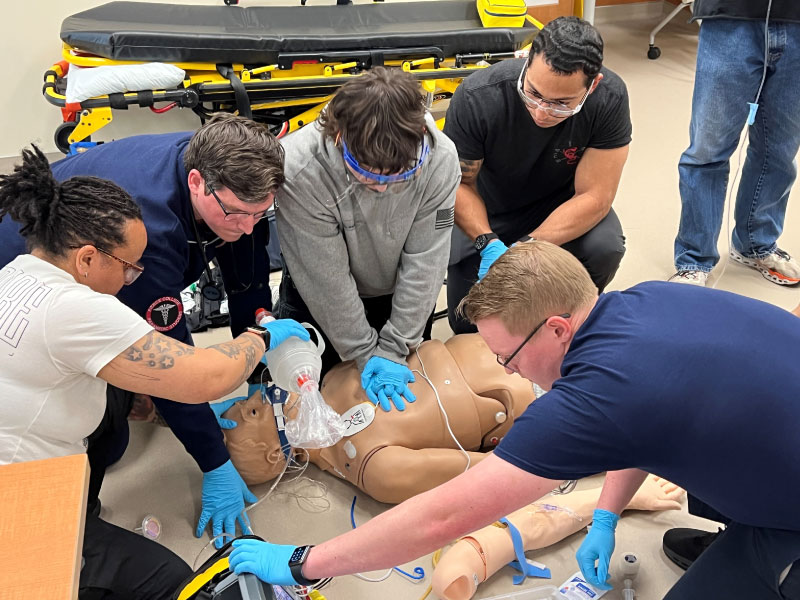 paramedic students surround a simulation dummy, providing emergency care