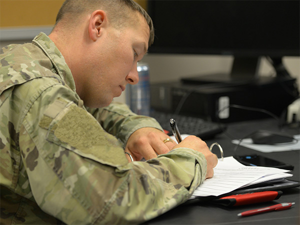 student in military uniform taking notes at desk