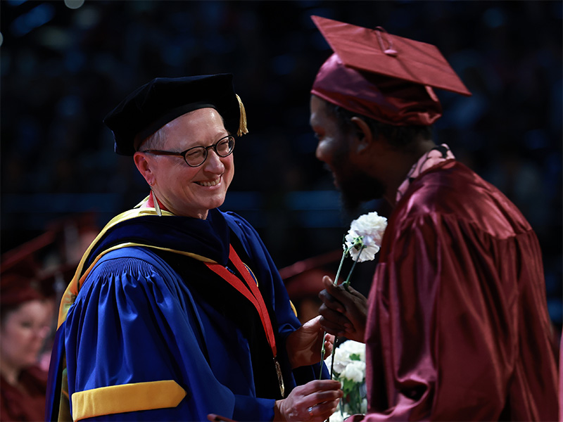 the college chancellor giving a graduate in cap and gown a carnation