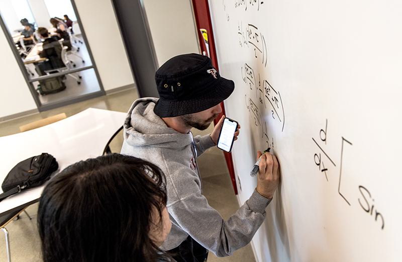 student solving math formula on whiteboard