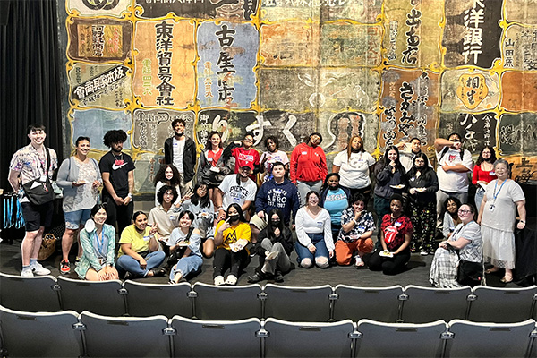 group of students pose in front of backdrop featuring colorful panels of japanese writing