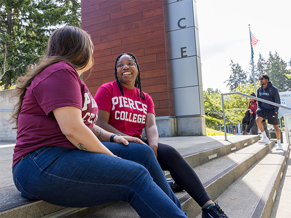 two students in pierce college shirts sitting outside on stairs