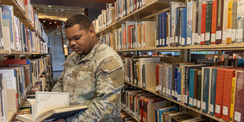 student in military uniform browsing bookshelves in library