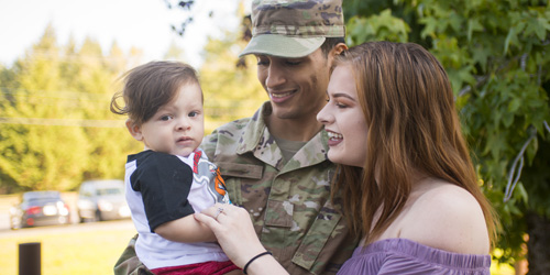 two parents, one in military uniform, hold their baby