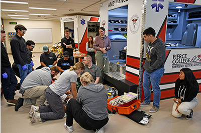 Pierce College students assembled in front of an EMT ambulatory simulator.