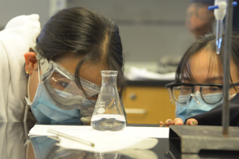 Two students examining a beaker during a chemistry lab experiment.