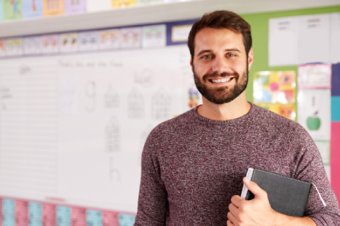 smiling teacher with book in front of bulletin board