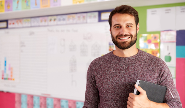 smiling teacher with book in front of bulletin board