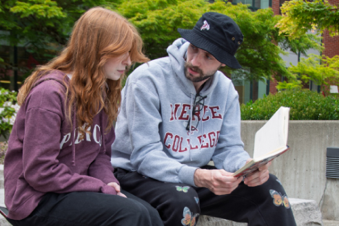 two students outside discussing a book