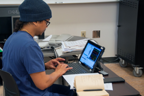 student in scrubs entering data into laptop