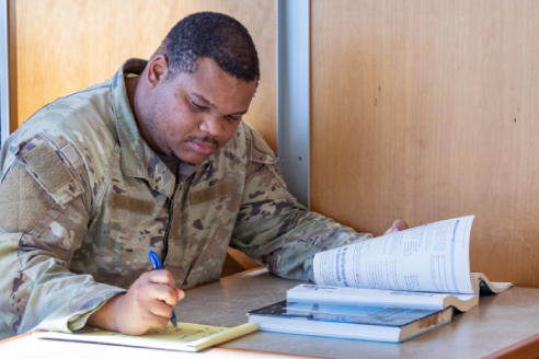 student in military uniform taking notes while reading textbook