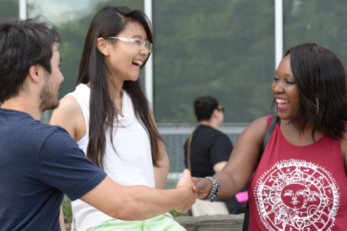two smiling students shaking hands along with a third student