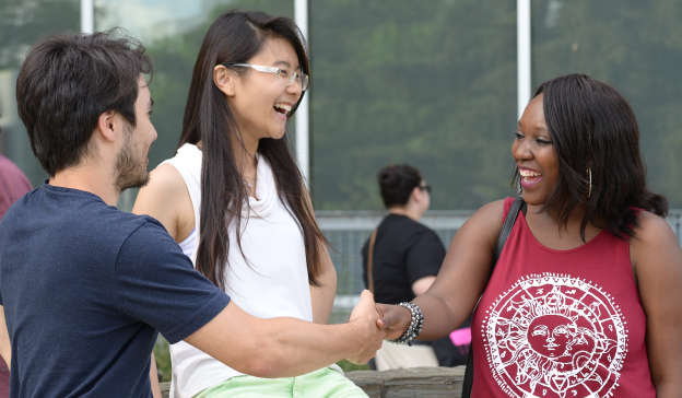 two smiling students shaking hands along with a third student