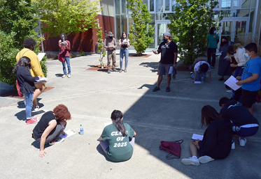 group of students seated outdoors in a circle on the ground
