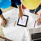 two people in hard hats viewing blueprints on paper and computer tablet