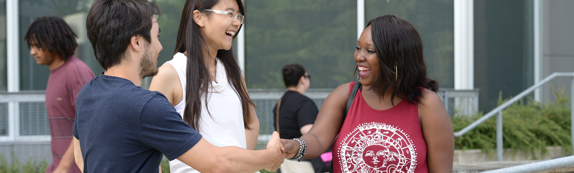 two students shaking hands in front of a third student