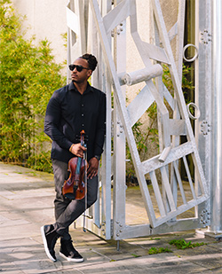 t-ray the violinist standing outside, holding a violin