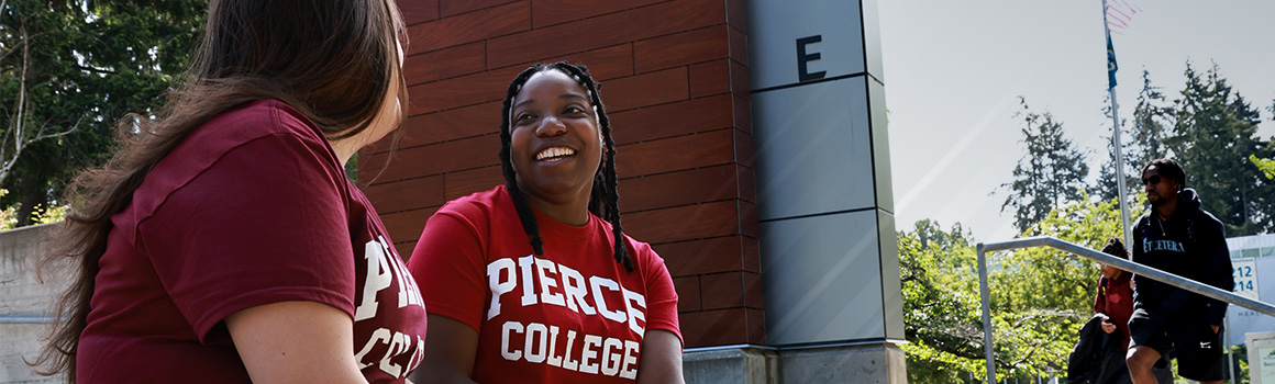 two students in pierce college shirts sit outside on fort steilacoom campus