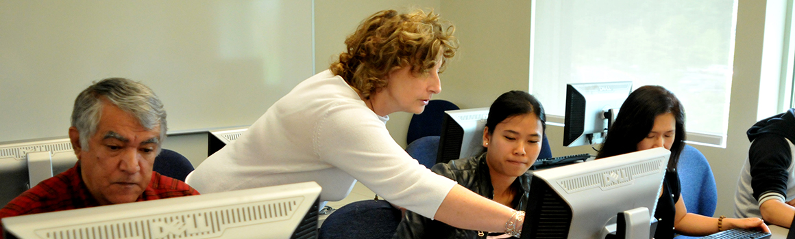 instructor guiding students in front of computers in a classroom