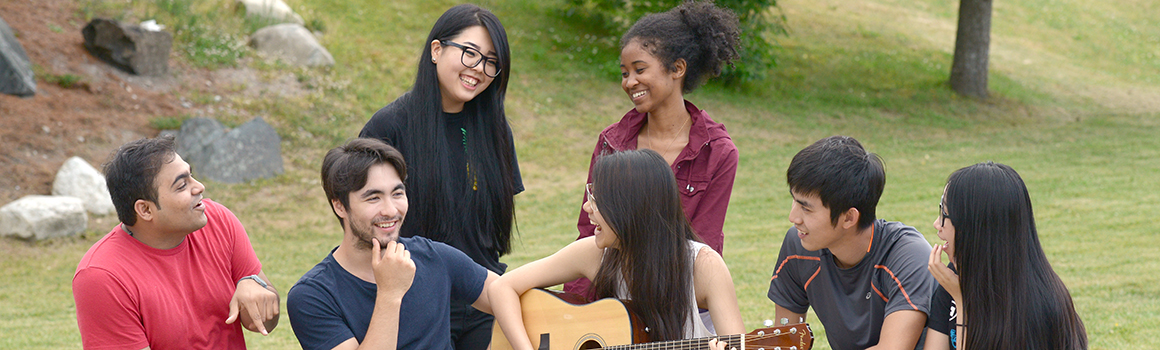 group of students sitting outside with guitar group of students sitting outside with guitar