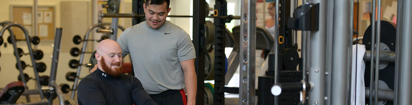 man working out at a rowing machine with trainer