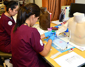 two nursing students in scrubs practicing with IVs two nursing students in scrubs practicing with IVs